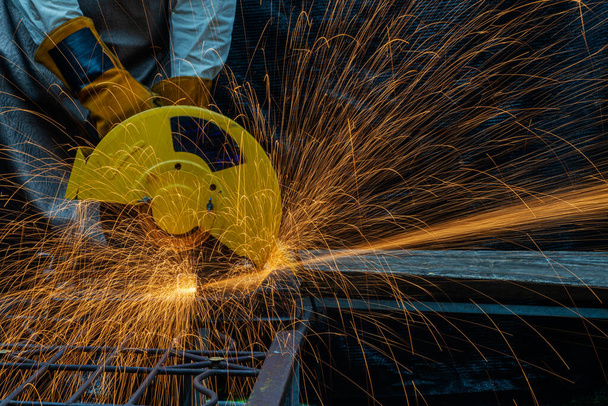 Hands of man with glove using electric steel cutter machine while working at workshop. Male cutting steel with sparks flying. Hard work in factory or garage industry in construction site concept. - Photo, Image