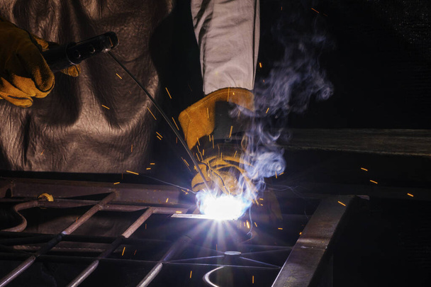 Ruka člověka nosit rukavice pracující s obloukem svařovací stroj svařovat ocel na venkovní. Svářečka svařuje ocelové výztuhy svařováním a jiskry. - Fotografie, Obrázek