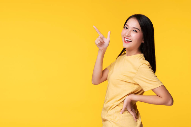 Vidám fiatal nő használja ujját mutató termék vagy üres másolás tér, miközben áll felett elszigetelt sárga háttér - Fotó, kép