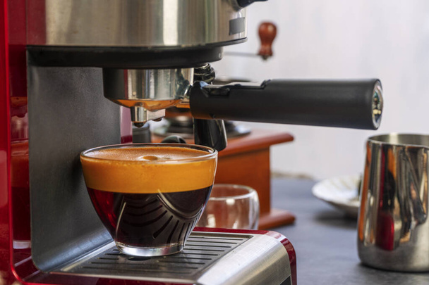 コーヒーマシンは、ホットエスプレッソや紅茶をグラスカップに入れ、テーブルの上にクリームを乗せてカフェに入れます。蒸し湯作りカプチーノのマグカップで午前中. - 写真・画像