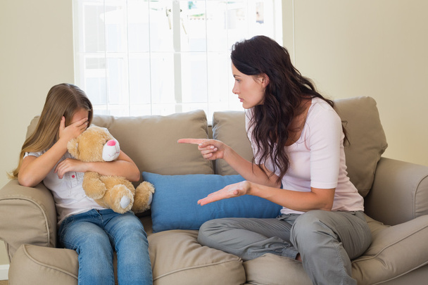 Woman pointing at scared daughter on sofa - Photo, Image