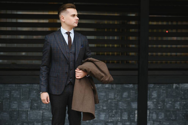 Portrait of handsome fashion businessman model dressed in elegant suit. Man posing on street background. Metrosexual - Фото, зображення