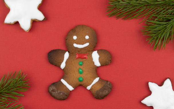 トウヒの枝で飾られた赤い背景のジンジャーブレッドの男性。伝統的なクリスマスジンジャーブレッドクッキー。休日は手作り。トップビュー、コピースペース - 写真・画像