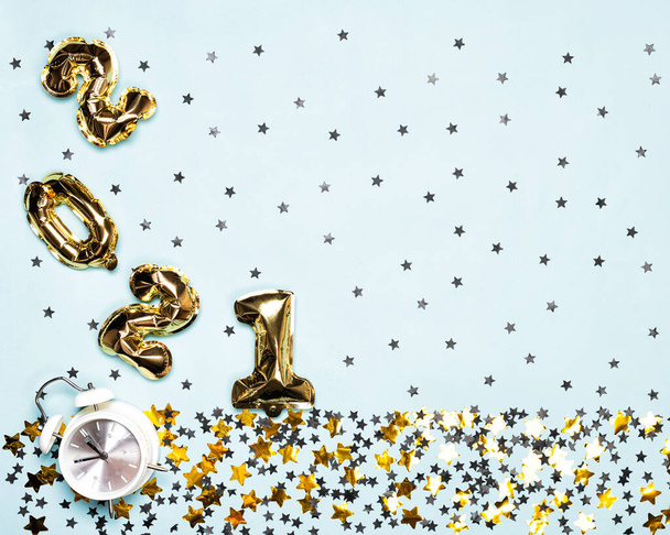 2021 ballonnen en wekker met zwarte en gouden sterren en cirkel confetti op de blauwe achtergrond. Kerst of Nieuwjaar feestelijk concept. Bovenaanzicht en vlakke lay. - Foto, afbeelding
