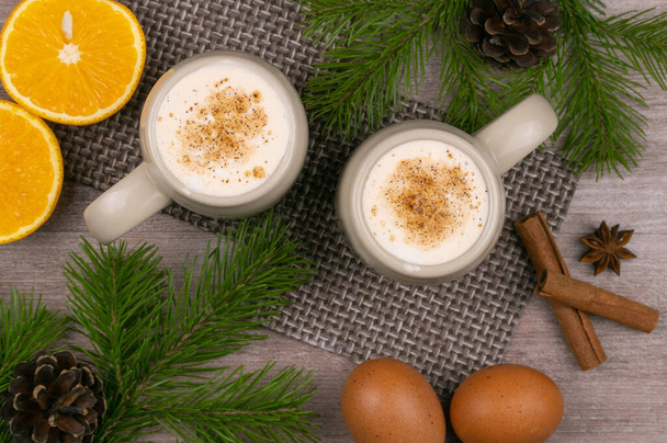 伝統的な休日は卵を飲む。生の鶏の卵と牛乳を使った甘い飲み物です。すりおろしたナツメグとシナモンとクリスマスカクテル。コーンのあるトウヒの枝の背景。トップビュー、コピースペース. - 写真・画像
