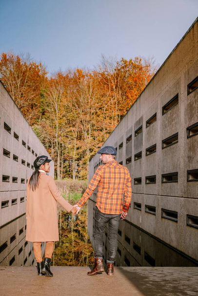 秋の間に森の中をハイキングするカップルの男性と女性秋の色とオレンジと赤の葉を持つ小さなストリーミングウォーター川ウォーターループボスフレヴォランドオランダ  - 写真・画像