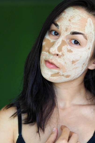  jeune femme brune avec un masque fait maison en argile sur son visage regarde dans le cadre - Photo, image