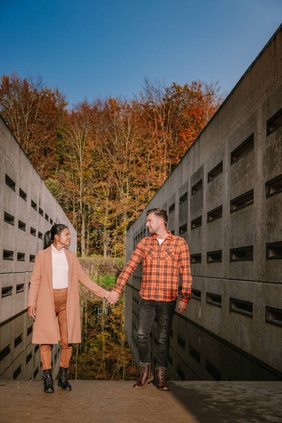 秋の間に森の中をハイキングするカップルの男性と女性秋の色とオレンジと赤の葉を持つ小さなストリーミングウォーター川ウォーターループボスフレヴォランドオランダ  - 写真・画像