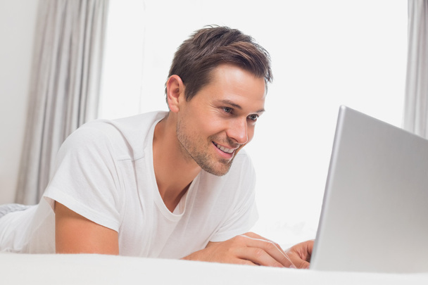 Relaxed casual man using laptop in bed - Zdjęcie, obraz