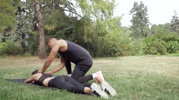 Muž dělá sportovní masáže žena po tréninku venku. Sportovní manuální terapie na trávě. Fitness trenér dělá manuální léčbu ženského sportovce. Fitness muž dělá svalové masáže - Záběry, video