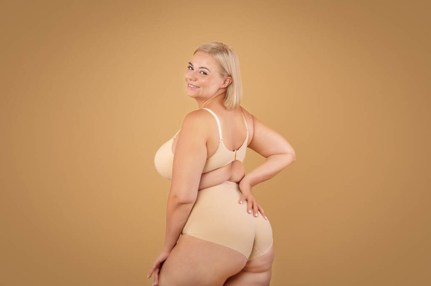 Tělo pozitivní. Krásná zakřivená žena pózování ve spodním prádle nad béžové studio pozadí - Fotografie, Obrázek