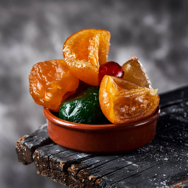 algumas frutas cristalizadas espanholas apetitosas, como cerejas de laranja, pêra, ameixa ou marrasquino, tipicamente comidas no Natal, em uma superfície de madeira cinza escuro rústico, contra um fundo cinza - Foto, Imagem
