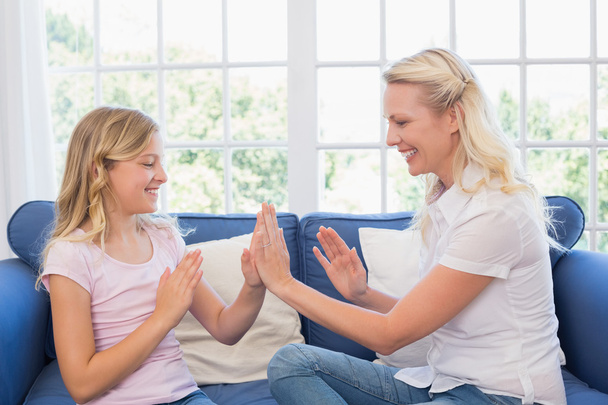 Mother and daughter playing clapping game on sofa - Foto, immagini