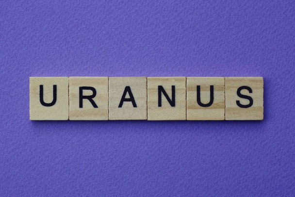 серое слово уранус маленькими квадратными деревянными буквами с черным шрифтом на сиреневом фоне - Фото, изображение