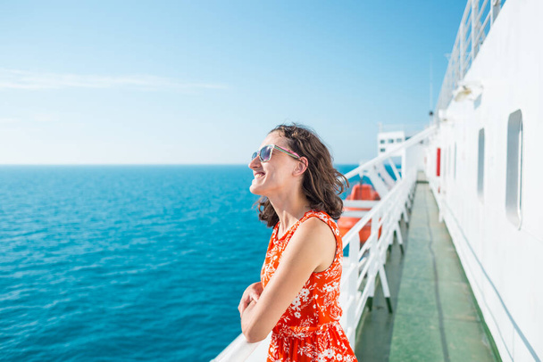Жінка пливе на круїзному кораблі, дівчина стоїть біля паркану на кораблі і дивиться на море, подорожуючи на поромі, брюнетка в літній сукні захоплюється океаном
. - Фото, зображення