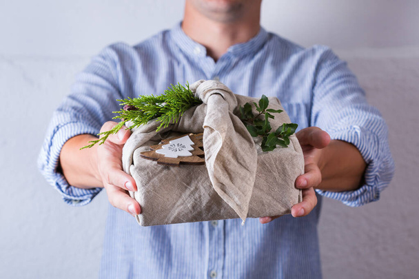 Creative zero waste Christmas concept. Hands giving handmade gift box wrapping in eco friendly traditional Japanese style furoshiki fabric - Φωτογραφία, εικόνα