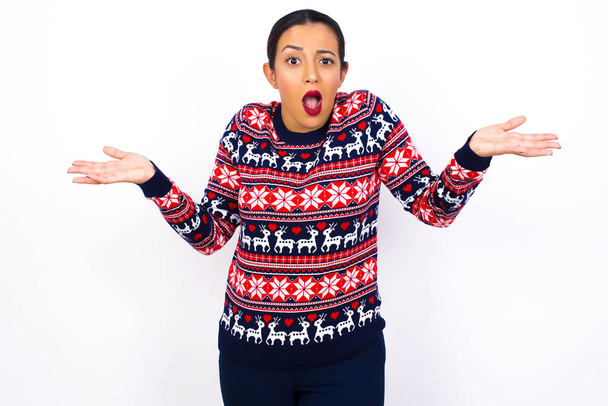 So what? Portrait of arrogant  Young beautiful Arab woman wearing Christmas sweater shrugging hands sideways smiling gasping indifferent, telling something obvious. - Photo, Image