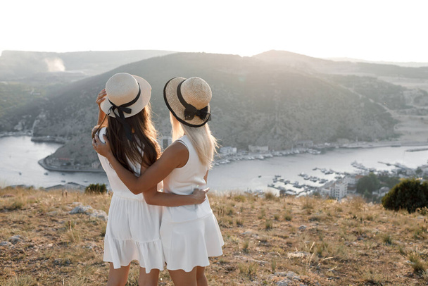 Two friends back view outdoor, Girls in dress and hat infront of the sea - Zdjęcie, obraz