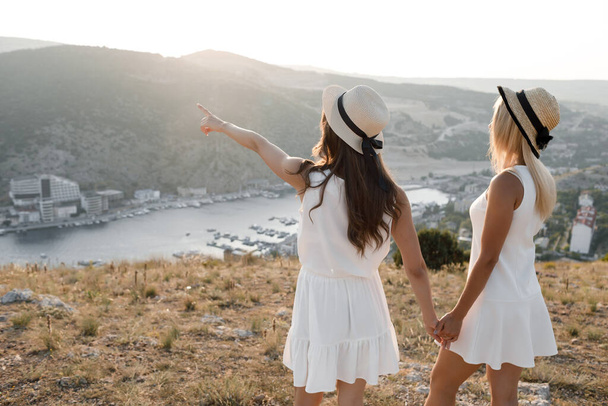 Two happy friends, tourism concept Summer vacation. Best friends in dress and hat. Showing the way by hand - Фото, изображение