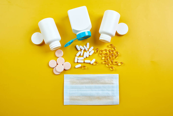 Platte lay van medische masker en pillen, visolie, vitaminen op gele achtergrond, coronavirus COVID-19 concept, Assorted farmaceutische pillen, tabletten en capsules, Immuunbooster. - Foto, afbeelding