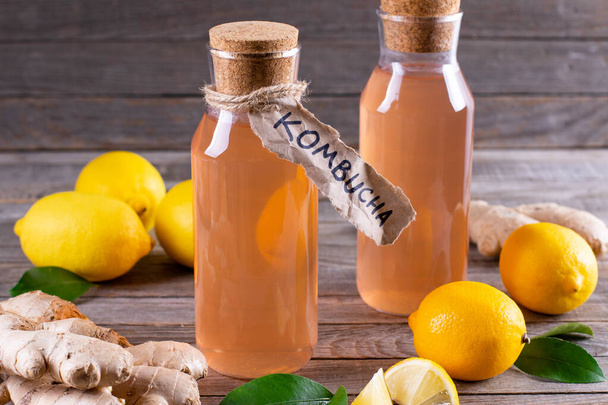 Kombucha or cider fermented drink. Cold tea beverage with beneficial bacteria, ginger, lemon on wooden background. For healthy nutrition. - Photo, image