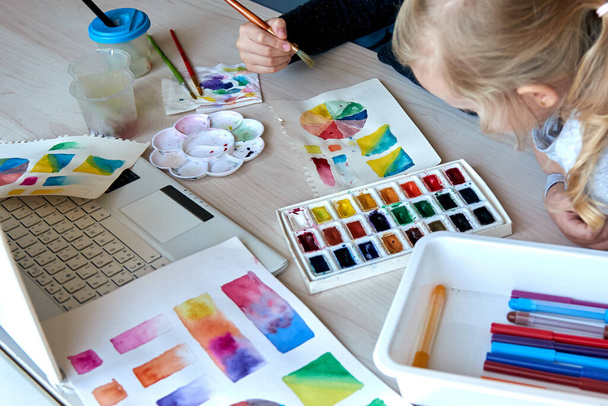 Children painting pictures with watercolor paints during art lesson. Pupils are concentrating on drawing with brush. Watercolor color wheel and palette. Color theory beginner hobby lessons - Fotoğraf, Görsel