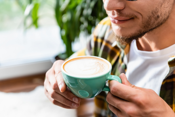 cropped view of blurred young man holding cup of coffee with foam - Photo, Image