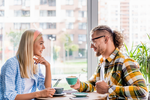 side view of cheerful stylish couple with coffee cup talking in cafeteria - Foto, Bild