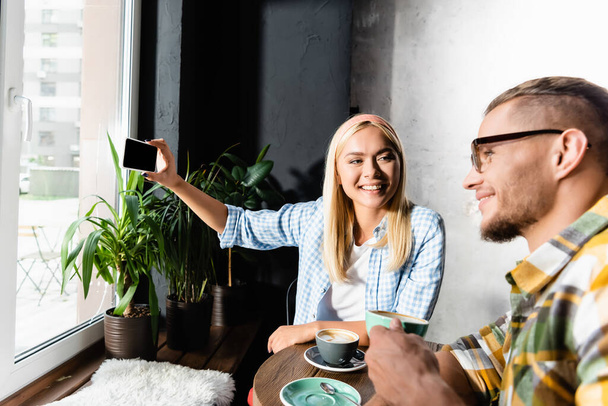 happy blonde woman taking selfie on smartphone with smiling man holding coffee cup on blurred foreground - Fotoğraf, Görsel