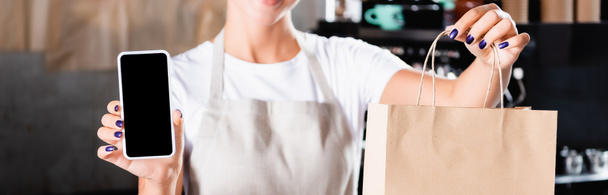 cropped view of waiter holding paper bag and smartphone with blank screen, banner - Photo, Image