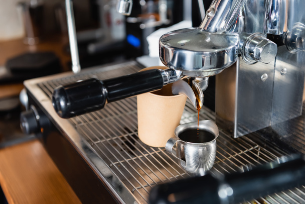 metallic mug with coffee near dispenser of professional coffee machine and disposable cup, blurred foreground - Photo, Image