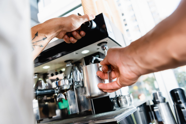 partial view of barista holding metallic milk mug near coffee machine steamer on blurred foreground - Photo, Image