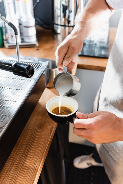 Kahve barmeninin metalik bardaktan kahve bardağına süt dökme görüntüsü. - Fotoğraf, Görsel