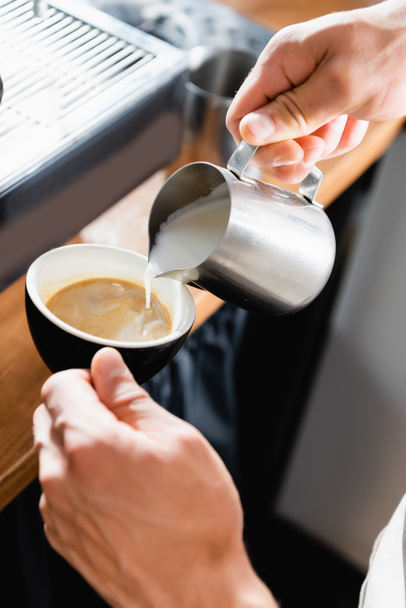 Kahve barmeninin metalik bardaktan kahve bardağına süt dökme görüntüsü. - Fotoğraf, Görsel