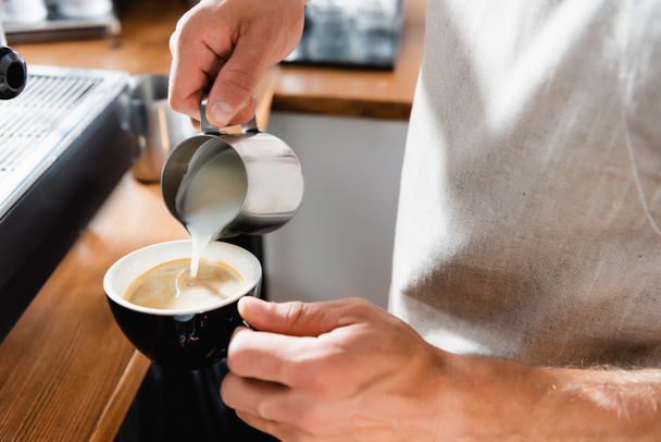 partial view of barista adding milk into cup of coffee  - Foto, afbeelding