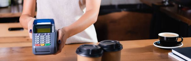 partial view of barista holding payment terminal near coffee to go on blurred foreground, banner - Photo, Image
