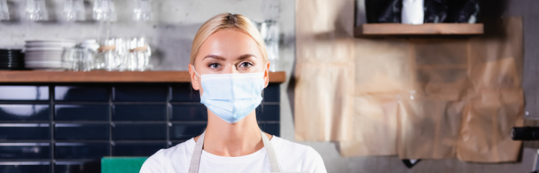 young blonde barista in medical mask looking at camera, banner - Photo, Image