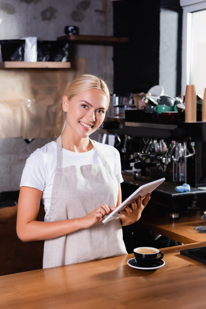 sorrindo loira barista usando tablet digital perto de xícara de café no balcão bar - Foto, Imagem