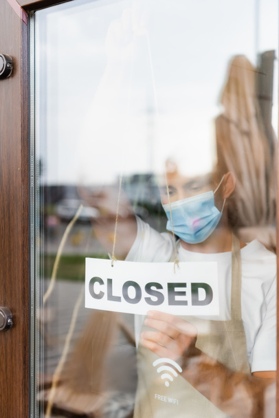 σερβιτόρος σε ιατρική μάσκα κρέμονται κάρτα με κλειστά γράμματα στην πόρτα του καφέ - Φωτογραφία, εικόνα