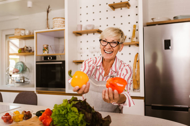 Ευτυχισμένη ηλικιωμένη γυναίκα που μαγειρεύει στη μοντέρνα κουζίνα της - Φωτογραφία, εικόνα