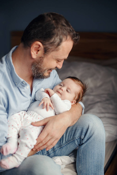 Middle age Caucasian father with sleeping newborn baby girl. Parent holding rocking child daughter son in hands. Authentic lifestyle parenting fatherhood moment. Family home life. - Photo, Image