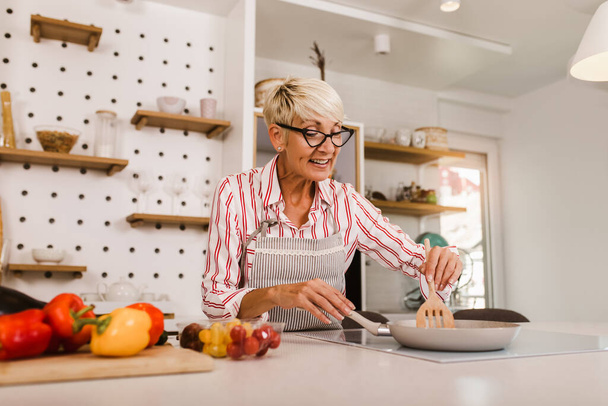 Щаслива старша жінка готує на своїй сучасній кухні
 - Фото, зображення