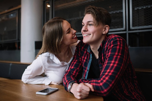 Positive man and woman wearing casual clothes smiling while sitting in cafe and laughing happily and discussing plans while resting in cafe - Φωτογραφία, εικόνα