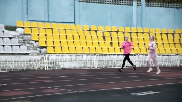 dwie pasujące białe bliźniaczki w odzieży sportowej biegające po torze stadionowym - Materiał filmowy, wideo
