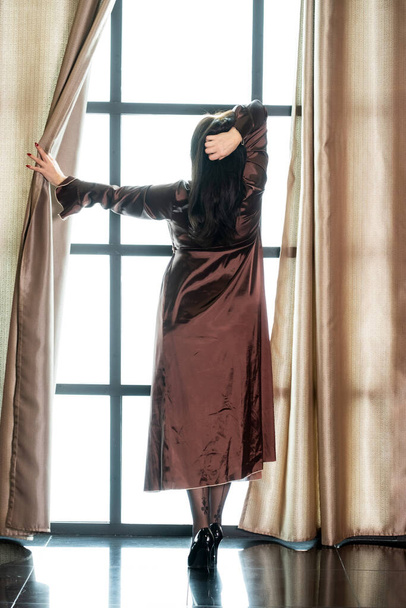 mujer en un peignoir largo cerca de una ventana grande en la mañana - Foto, Imagen