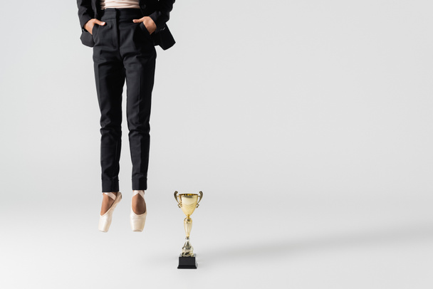 abgeschnittene Ansicht einer afrikanisch-amerikanischen Geschäftsfrau in Spitzenschuhen, die in der Nähe einer goldenen Tasse auf grau springt - Foto, Bild