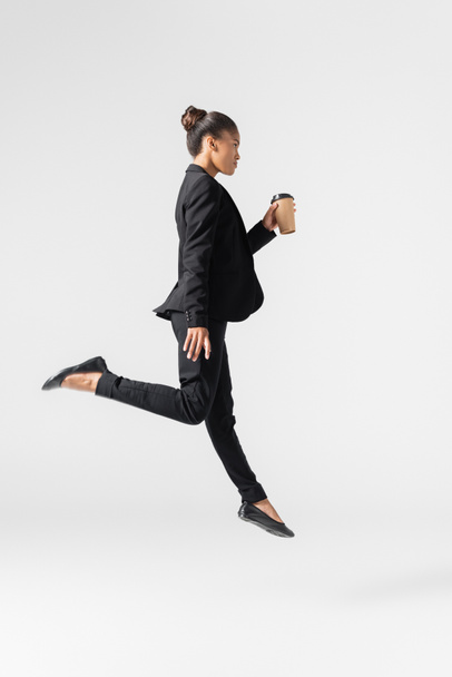 side view of african american businesswoman performing ballet with paper cup isolated on grey - Foto, immagini