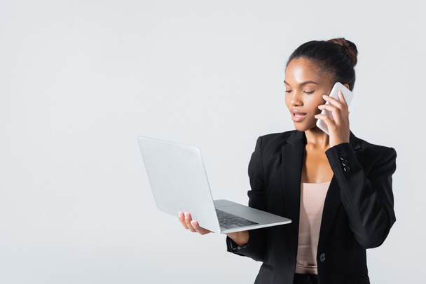 african american businesswoman with laptop talking on smartphone isolated on grey - Φωτογραφία, εικόνα