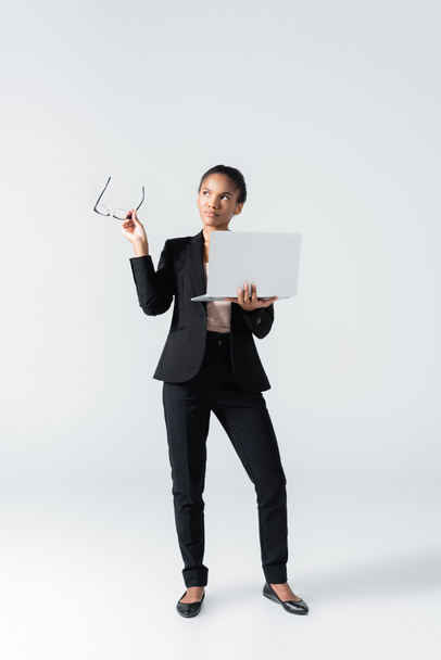 chère femme d'affaires afro-américaine avec lunettes et ordinateur portable isolé sur gris - Photo, image