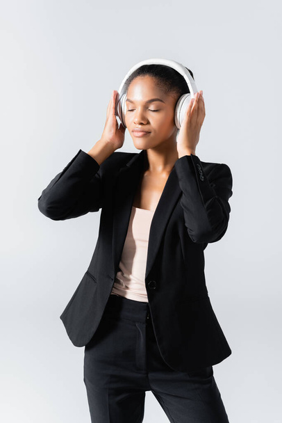 african american businesswoman listening music in headphones isolated on grey - Zdjęcie, obraz